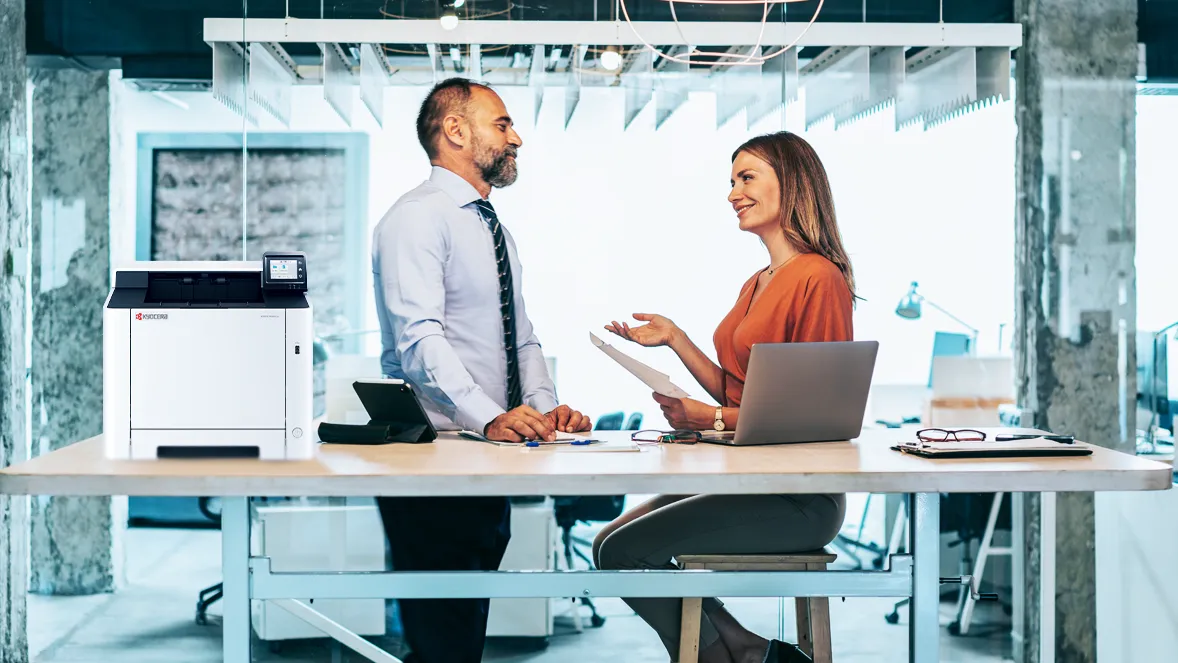 Man and Woman Chatting in Modern Office Environment with Kyocera Device on Desk