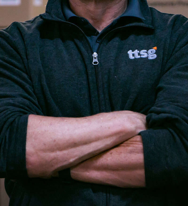 ttsg-bob TTSG employee with arms crossed wearing a TTSG-branded jacket